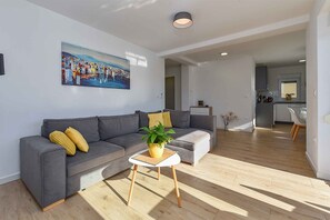 A modern living room with a grey sofa, a small white table with a plant, and a painting on the wall. - Holiday flat with full amenities (Štinjan)