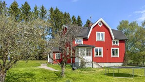 Ein rotes Haus mit einem geneigten Dach, einer kleinen Veranda und einem Rasen.