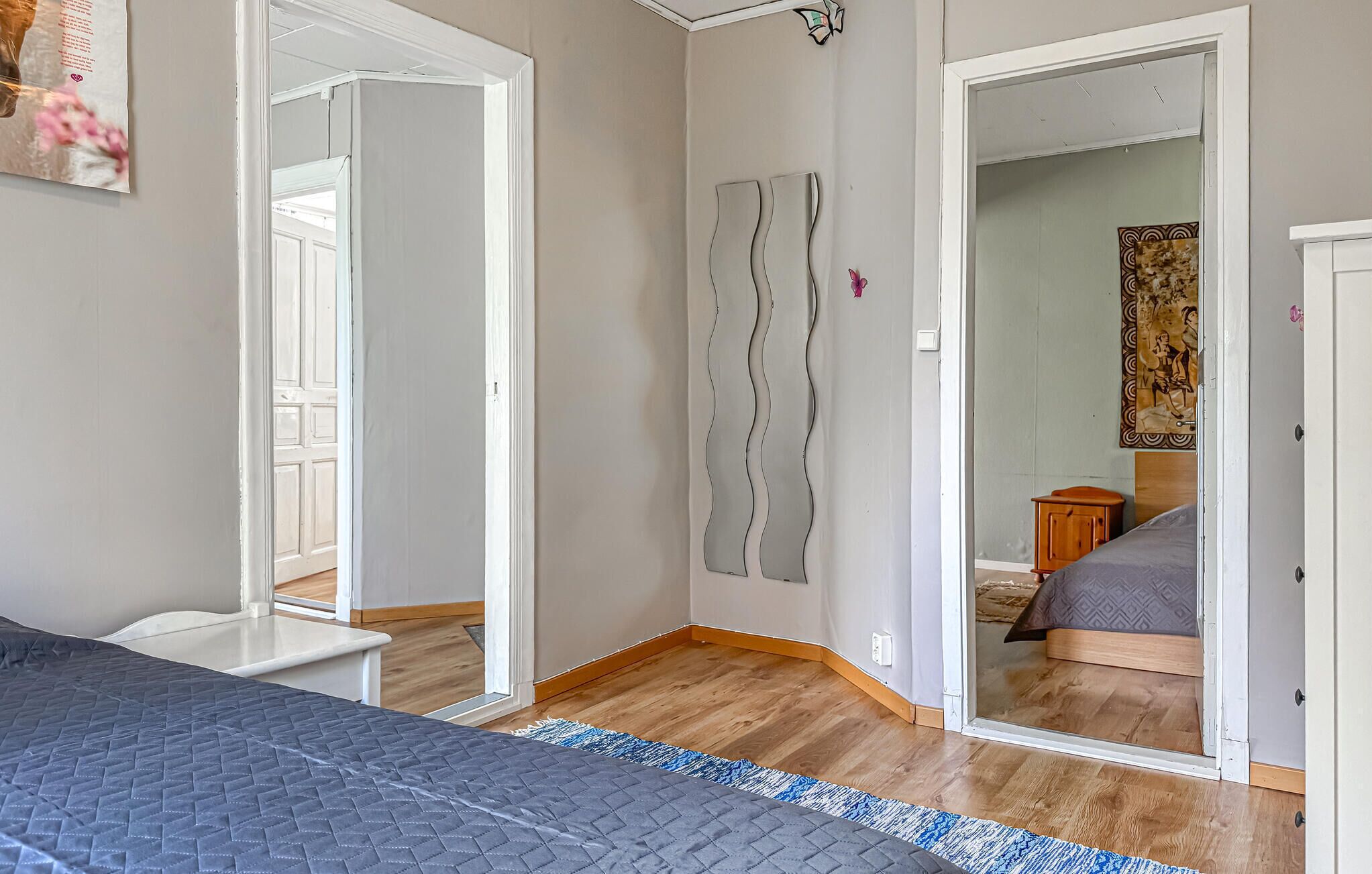 Een slaapkamer met een bed, een garderobe, een spiegel en een deur naar een andere kamer.