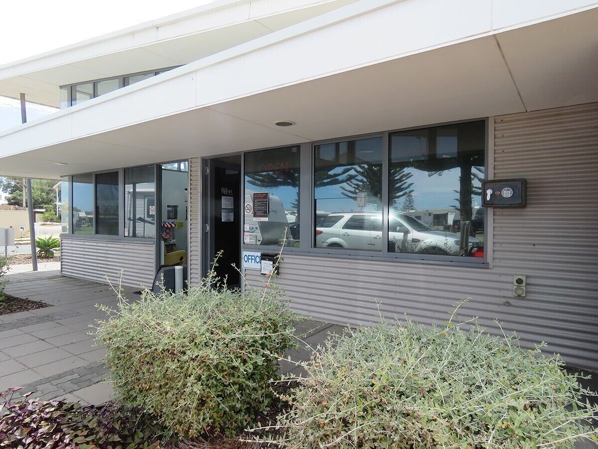 A modern building with a glass entrance, a visible office sign, and a security keypad on the door.