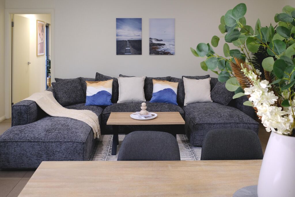 A living room with a grey sofa set, a wooden coffee table, and a vase with white flowers.