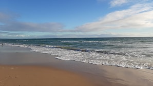Una playa con olas, cielo despejado y horizonte lejano.