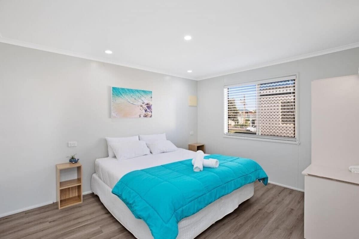 Un dormitorio moderno con una cama, una mesita de noche, una ventana con persianas y una obra de arte colgada en la pared.