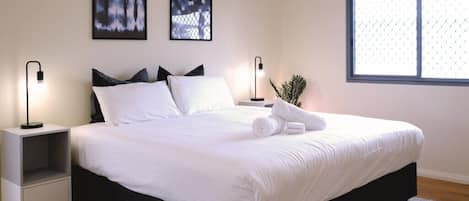 A neatly made bed with white linens, two bedside tables with lamps, and two framed pictures on the wall.