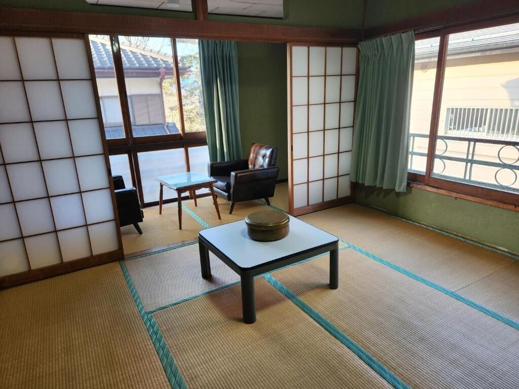 Um espaço com esteiras de tatame, uma mesa baixa, uma cadeira e uma porta deslizante.