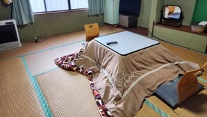 Una habitación con esteras de tatami, una cama, un escritorio, una silla, un televisor y un refrigerador pequeño.