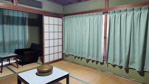 Una habitación japonesa tradicional con suelo de tatami, una mesa baja con un objeto redondo, una puerta corredera y un ventanal con cortinas verdes.