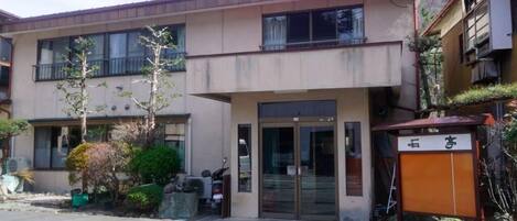 Un edificio de dos plantas con fachada plana, ventanas amplias y entrada protegida por un portón.