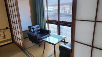 Una habitación japonesa tradicional con suelo de tatami, una butaca de cuero negro, una mesita y un puertas correderas.
