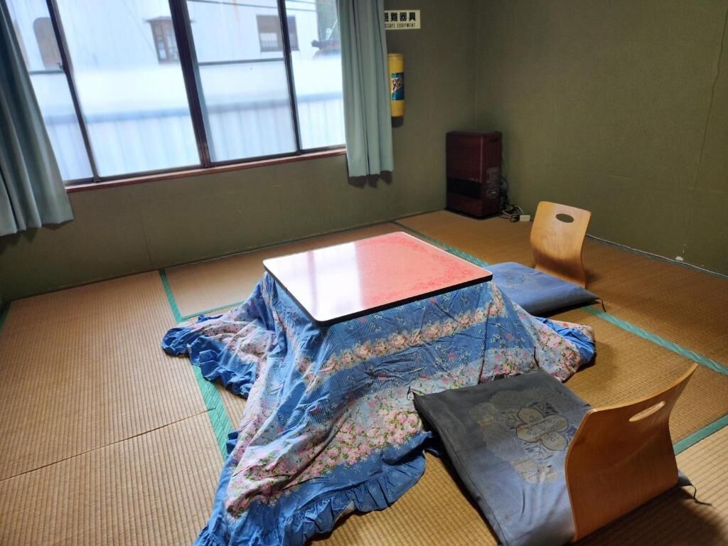 Een kamer met tatami matten, een bed, kussens, een tafel en een stoel.