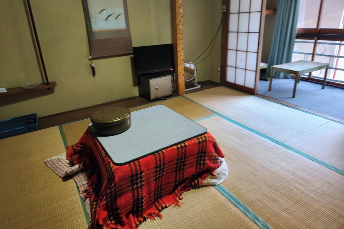 Ein Raum mit Tatami-Matten, einem niedrigen Tisch, einem Fernseher und einer Schiebetür.