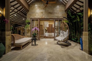 A spacious room with a large bed, a hanging chair, and a small table. There are plants and a ceiling fan. - Orchid Garden Villa (Ubud)