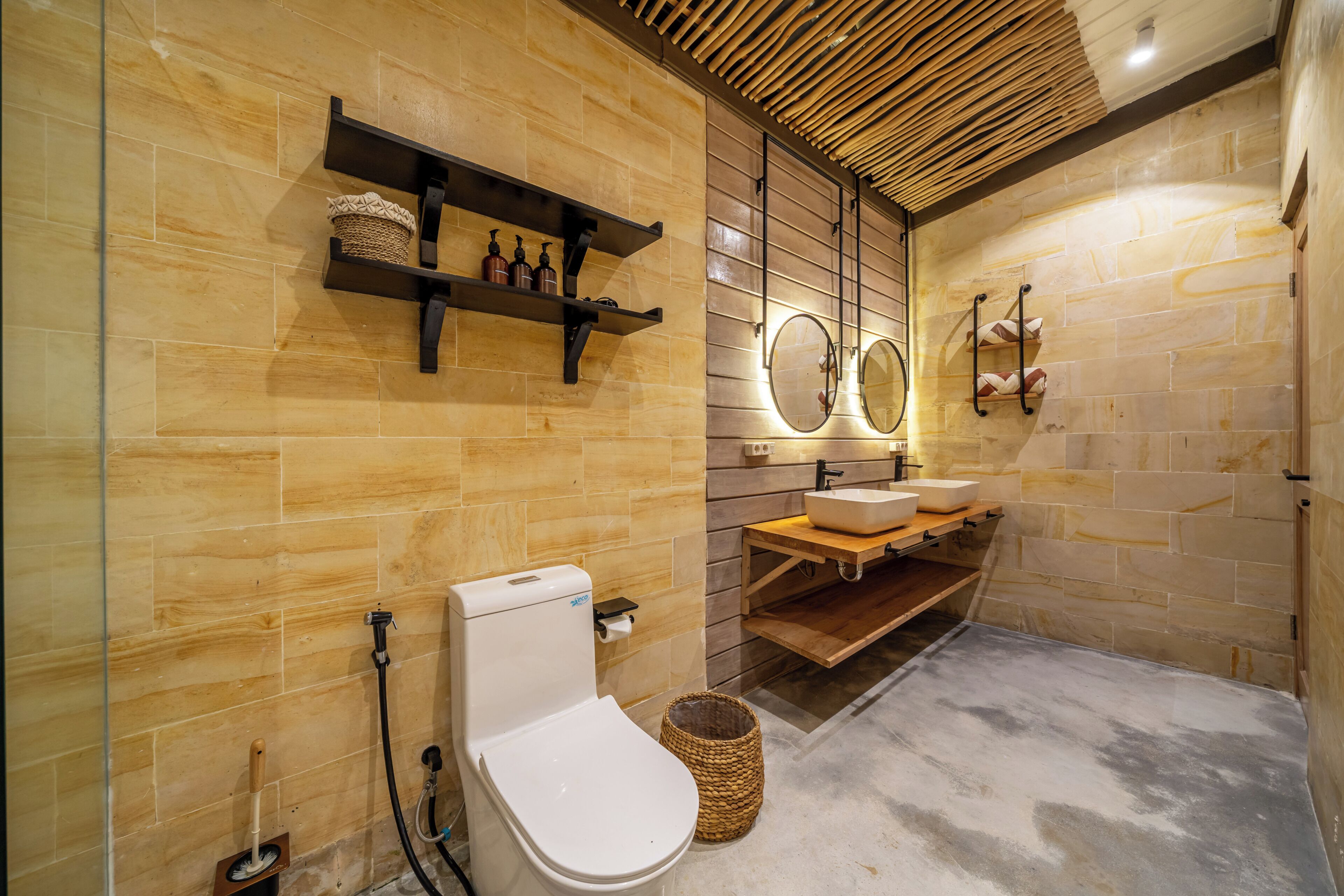 A modern bathroom with a wooden floor, a toilet, a sink with a mirror, and shelves with toiletries.