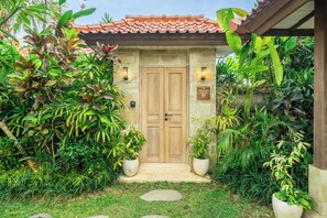 Un ingresso in pietra con una porta di legno, circondato da rigogliosa vegetazione tropicale.