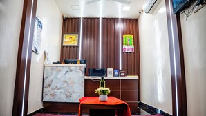 A reception area with a marble wall, a reception desk, a small table with a vase, and a ceiling fan. - V V Residency (Thanjavur)