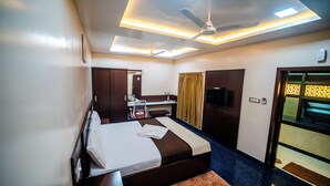 A hotel room with a bed, a desk, a ceiling fan, and a TV. - V V Residency (Thanjavur)