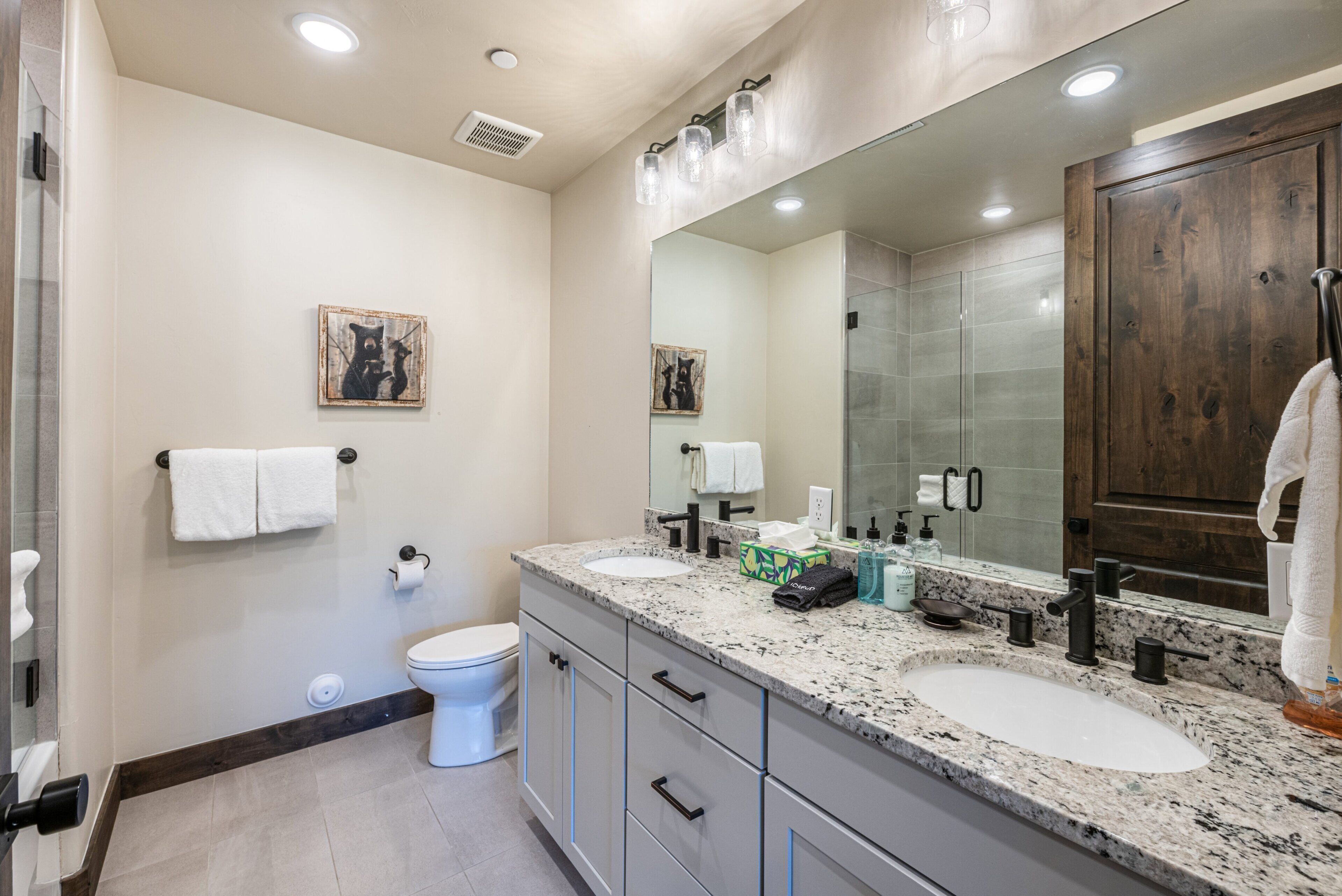 A modern bathroom with two sinks, a large mirror, and a toilet.