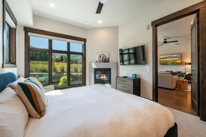 Quarto com cama grande, lareira, TV e vista para o exterior.