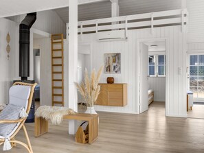 Ein geräumiger Raum mit hoher Decke, einer Holzleiter, einem Korbstuhl, einem Holztisch und Blick durch eine geöffnete Tür.