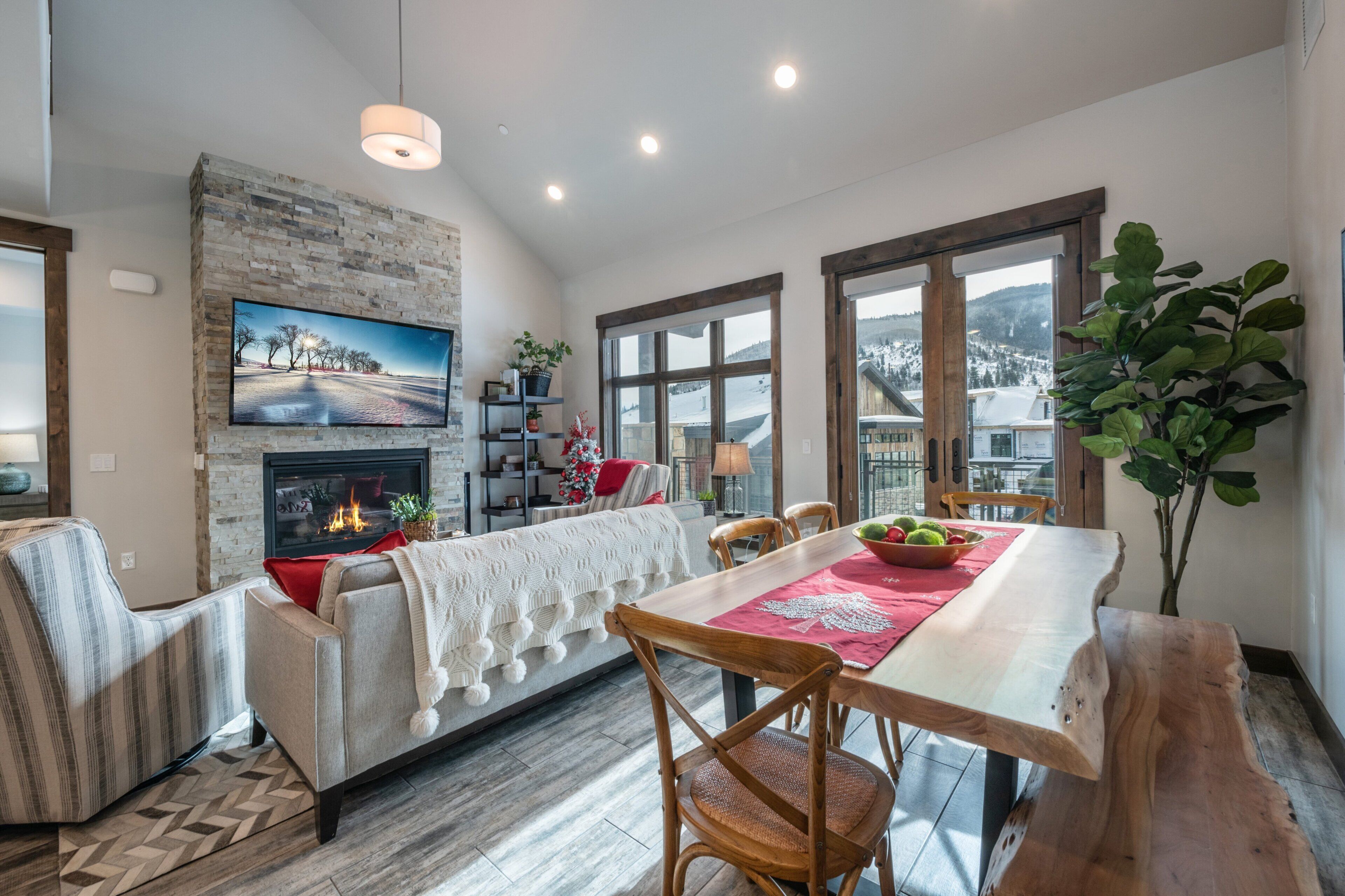 A modern living room with a fireplace, a dining table with chairs, and a large window with a view.