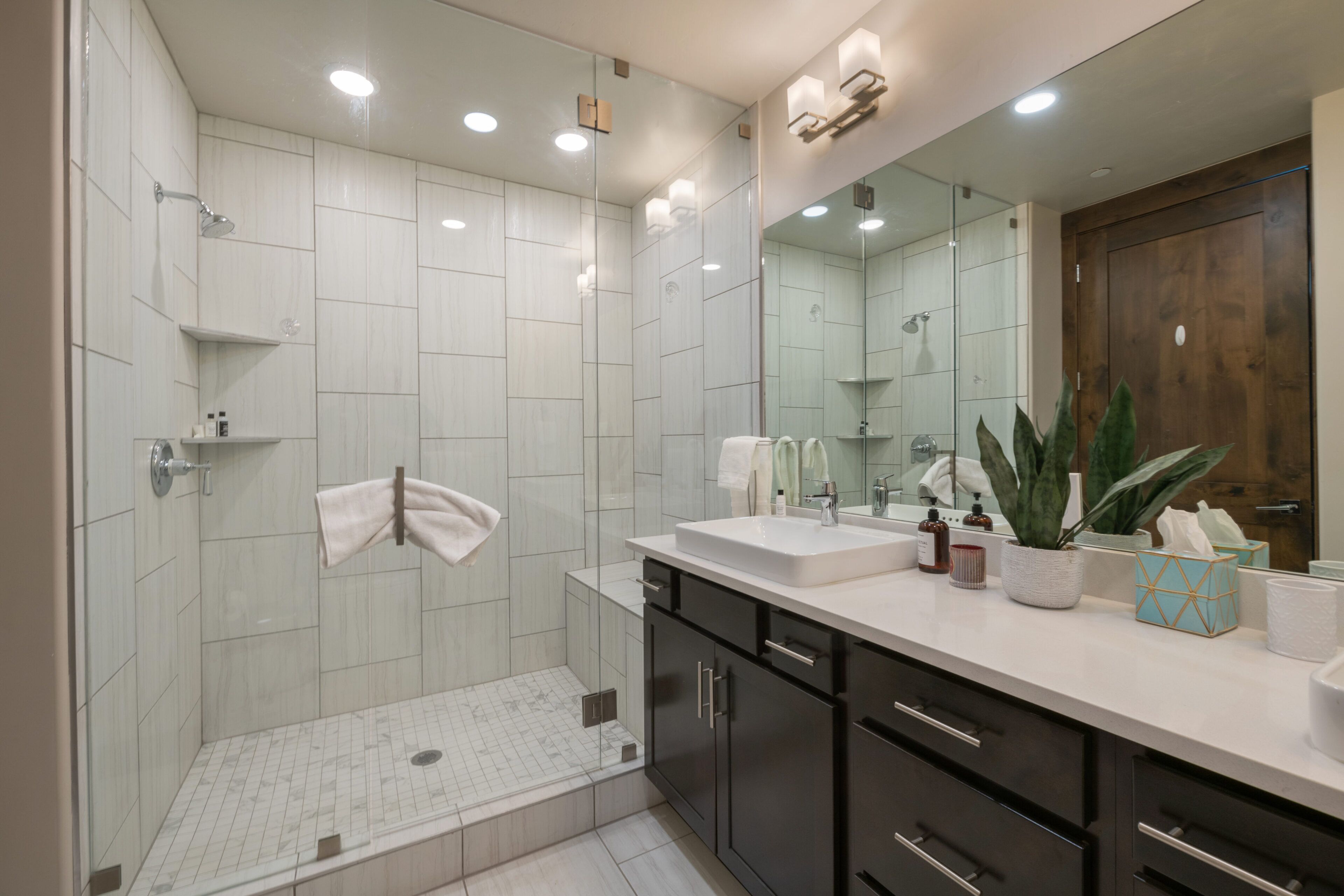 Een moderne badkamer met een douche met glazen wand, een grote spiegel en een wastafel met aanrecht.