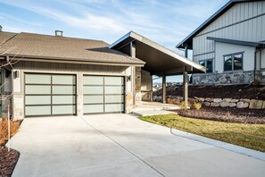 Ein modernes, zweistöckiges Haus mit Garage, Steinunterbau und überdachter Terrasse.