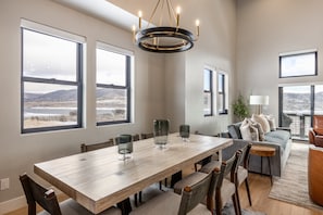 A dining area with a wooden table, chairs, and large windows with a view of the landscape. - Deer Valley East Perfect for Groups | 5BR w/ Game Room + Hot Tub (Heber City)