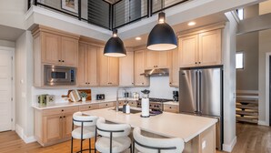 Una cucina moderna con mobili in legno, elettrodomestici in acciaio inossidabile, un'isola centrale con sgabelli da bar e illuminazione a sospensione.