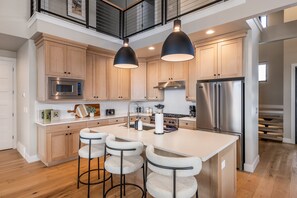 A modern kitchen with wooden cabinets, stainless steel appliances, a central island with bar stools, and pendant lighting. - Deer Valley East Perfect for Groups | 5BR w/ Game Room + Hot Tub (Heber City)