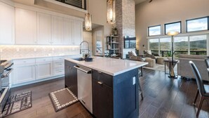 A modern kitchen with a central island, built-in appliances, and a dining area with a view. - Spacious Retreat | 5 King Beds | Hot Tub & Views (Deer Valley)