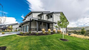 A modern two-story house with a covered porch, a stone foundation, and a well-maintained lawn. - Spacious Retreat | 5 King Beds | Hot Tub & Views (Deer Valley)