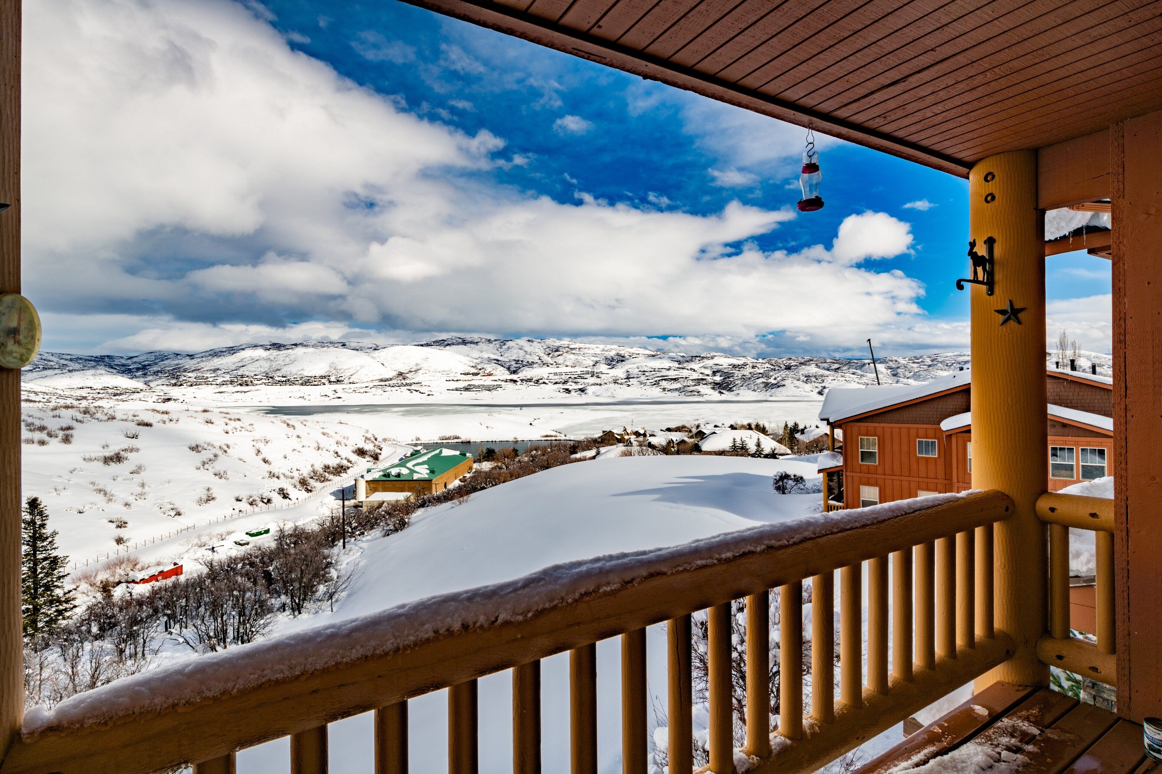 Un balcon en bois donnant sur un paysage enneigé, un ciel dégagé et une vue lointaine d’un bâtiment doté d’un toit végétalisé.