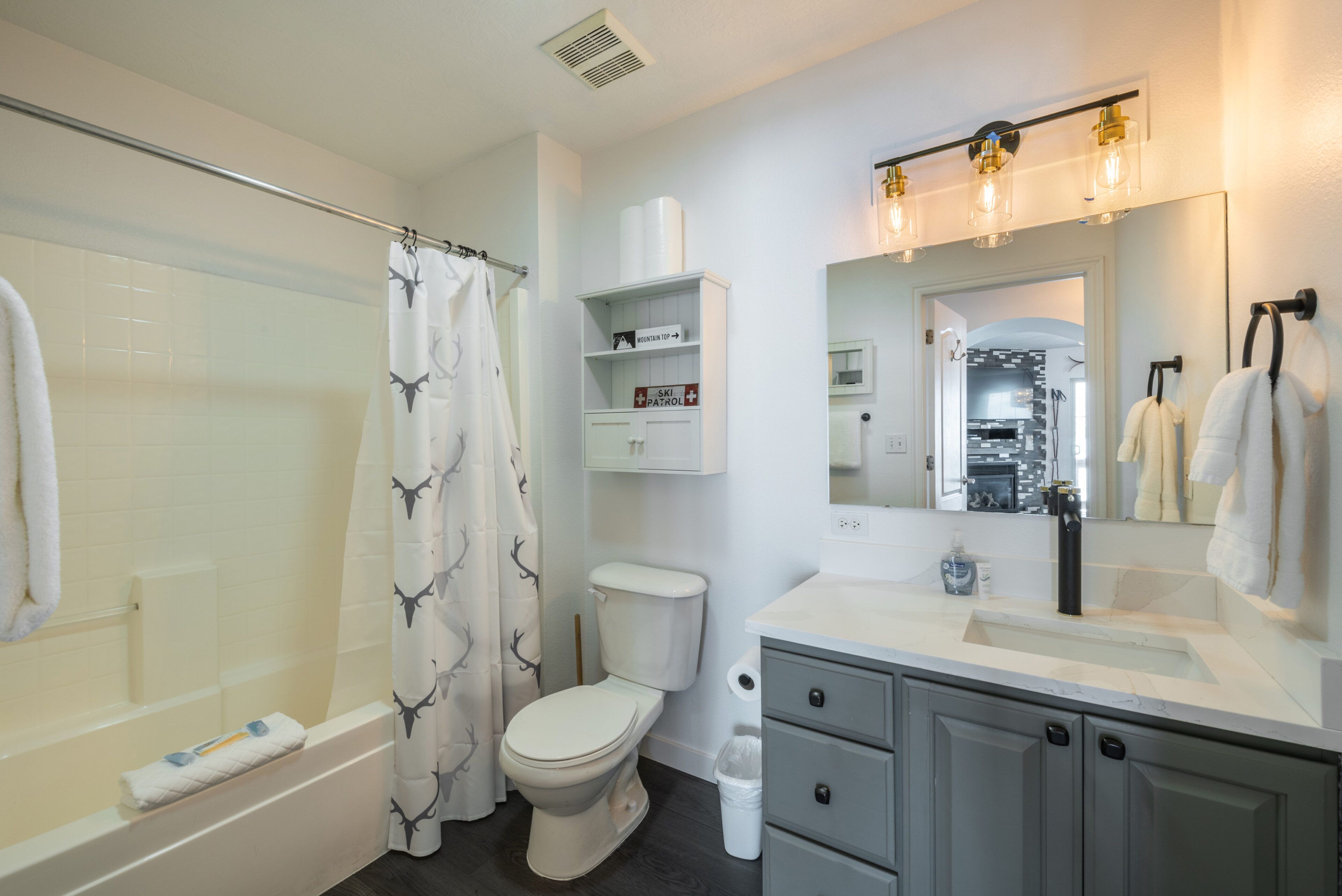 A bathroom with a shower, toilet, vanity, and a mirror with lights.
