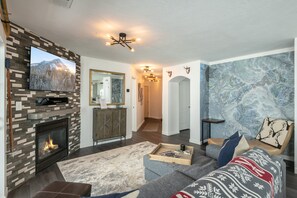 Ein Wohnzimmer mit Kamin, einem an der Wand montierten Fernseher, einer Couch und einer Wand mit Muster.