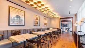 A restaurant with wooden tables and chairs, a high ceiling with circular light fixtures, and framed artwork on the walls.