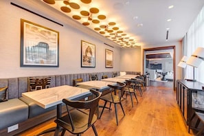 Un ristorante con tavoli e sedie in legno, un soffitto alto con lampade circolari e opere d'arte appese alle pareti.