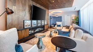 A modern living room with a wooden wall, a flat-screen TV, framed artwork, a sofa, a coffee table, and a lamp.