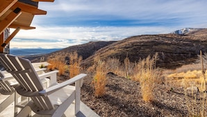 Eine Holzterrasse mit Adirondack-Stühlen mit Blick auf eine gebirgige Landschaft.