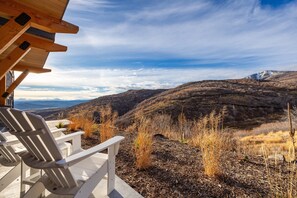 Eine Holzterrasse mit Adirondack-Stühlen mit Blick auf eine gebirgige Landschaft.