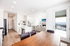 Eine moderne Küche mit weißen Schränken, ein Essbereich mit Holztisch und ein Wohnbereich mit Sofa und Blick ins Freie.