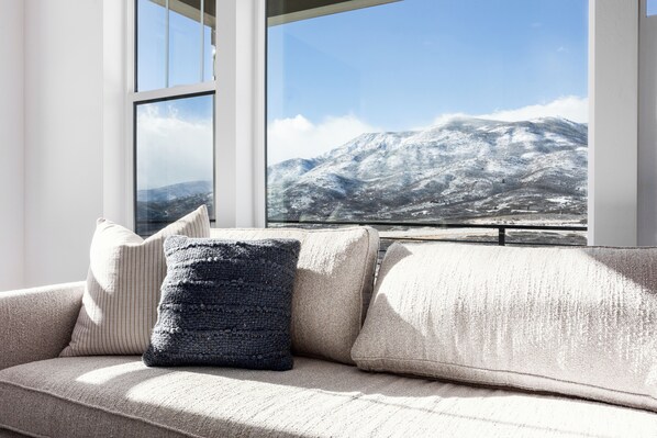Ein modernes Wohnzimmer mit einem großen Fenster mit Blick auf eine verschneite Berglandschaft.