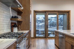 A kitchen with a stove, wooden cabinets, and a view of a snowy mountain through a glass door. - Luxury Ski Estate | Free Shuttle | Jordanelle Views (Heber City)