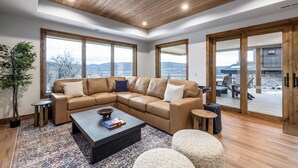 Ein modernes Wohnzimmer mit einem Ecksofa, einem Couchtisch und einem großen Fenster mit Blick auf die Berge.