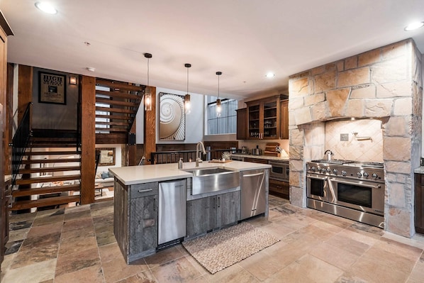 A modern kitchen with a central island, stainless steel appliances, and a stone fireplace. - Experience luxury in this 3BR, 3.5BA loft in Deer Valley, Park City, with stunning mountain views. (Park City)