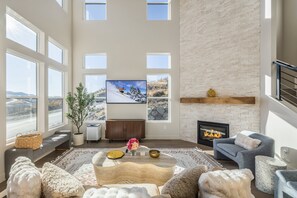 Ein geräumiges Wohnzimmer mit großen Fenstern, einem Kamin und einem an der Wand befestigten Fernseher.