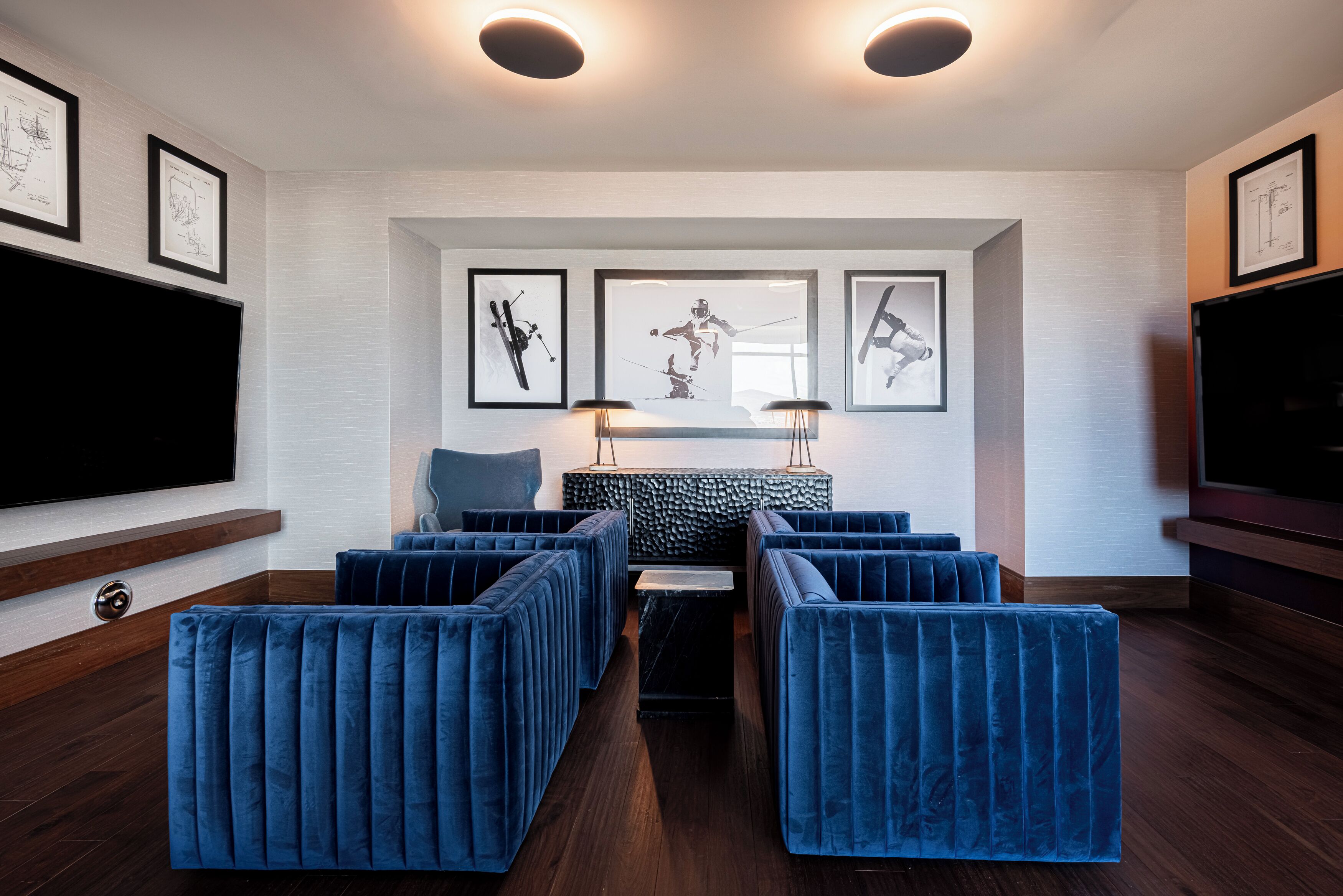 Een moderne woonkamer met een grote flatscreen televisie, beklede zitplaatsen in blauw, lijstwerken aan de muren en een accentmuur met patroon.