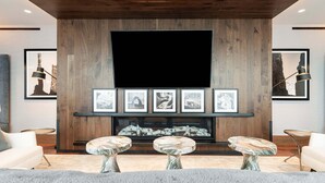A modern living room with a large flat-screen TV, wooden wall paneling, a fireplace, and marble-topped coffee tables. - 1BR in DV East, Steps to Gondola Ski-in/out, Amenities (Park City)