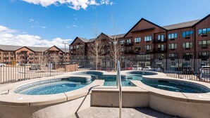 A pool area with multiple hot tubs, a fence, and a building with balconies in the background. - 1BR in DV East, Steps to Gondola Ski-in/out, Amenities (Park City)