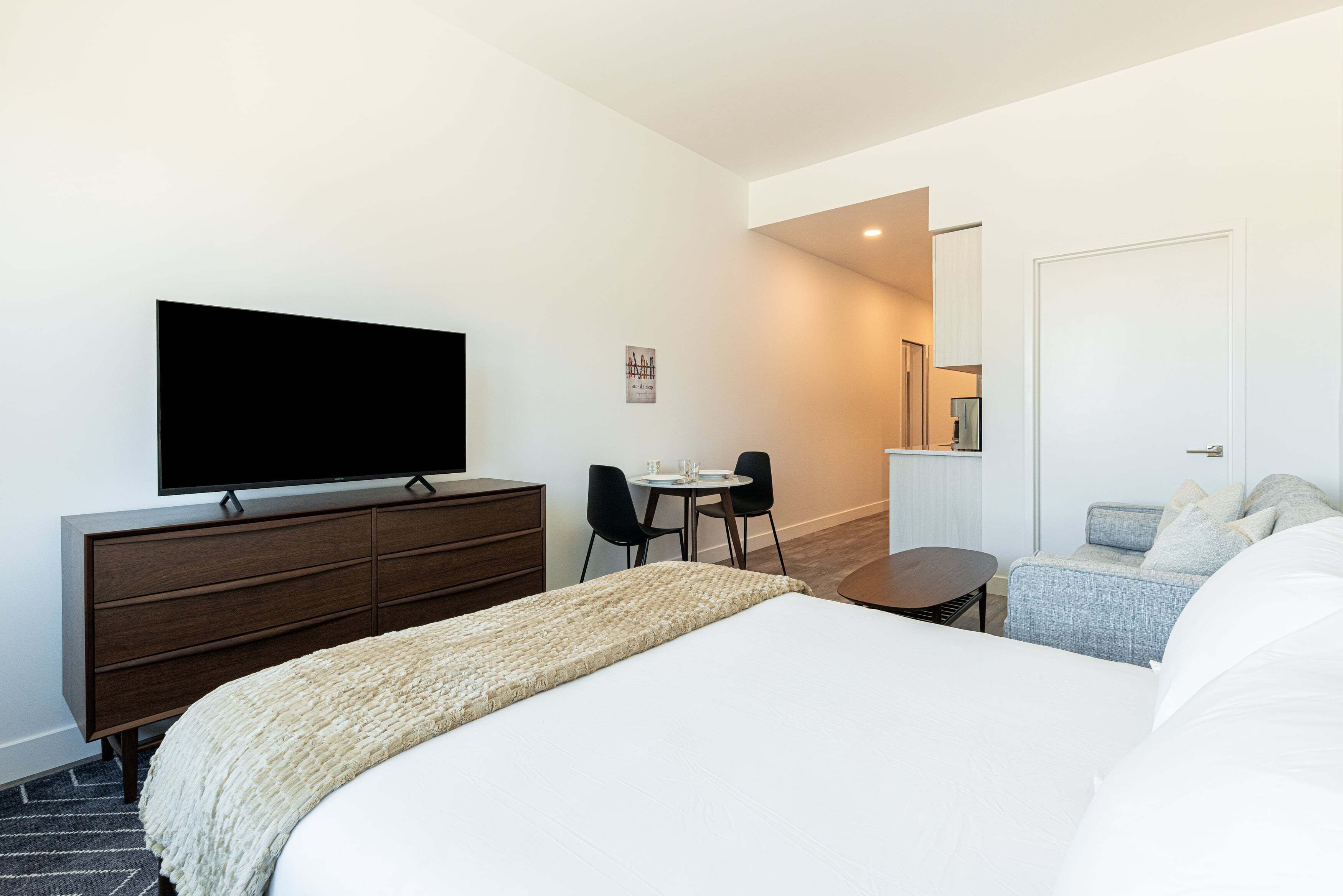 A hotel room with a bed, a TV on a dresser, a desk with chairs, and a sofa.