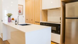 Eine moderne Küche mit weißen Schränken, einem Edelstahl-Kühlschrank, einem eingebauten Backofen und einem Spülbecken mit Blumen in einer Vase.